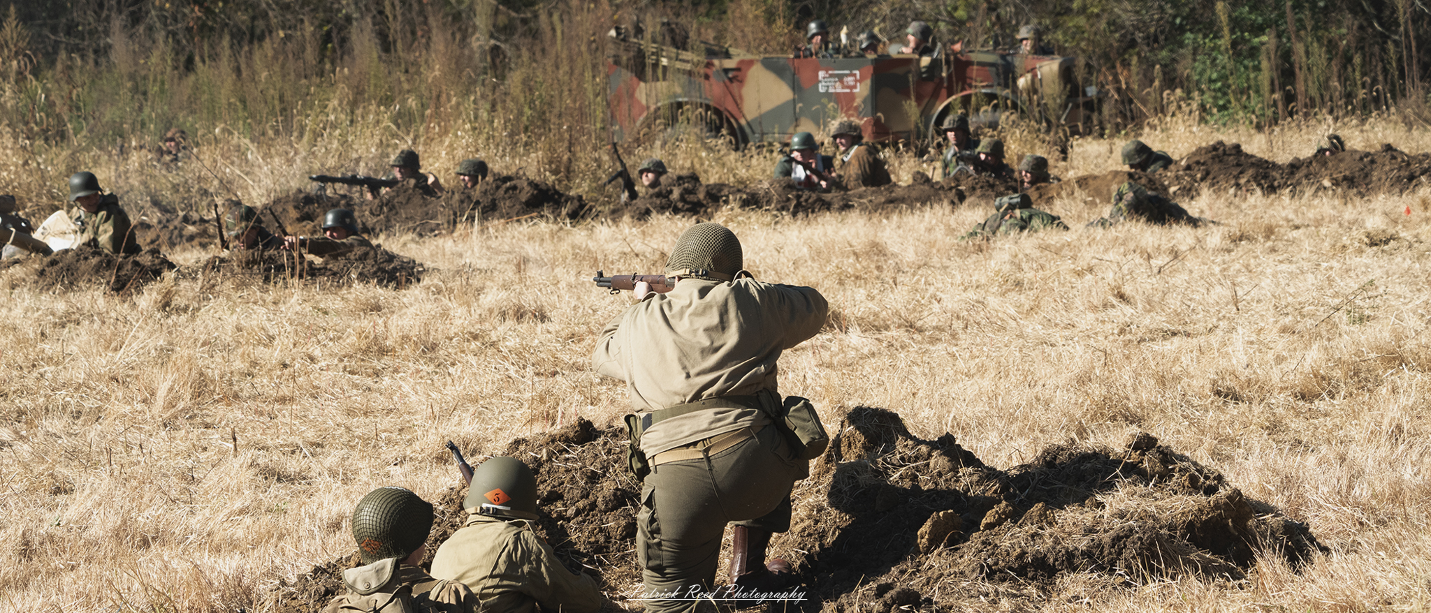 An American GI in full World War II combat gear, kneeling and firing a rifle on a battlefield. The soldier is focused and determined, his M1 Garand rifle aimed at the enemy. Dust and debris swirl around him, while the battlefield stretches out with scattered signs of conflict in the background. His helmet, uniform, and gear show signs of wear, reflecting the intensity of the combat zone.